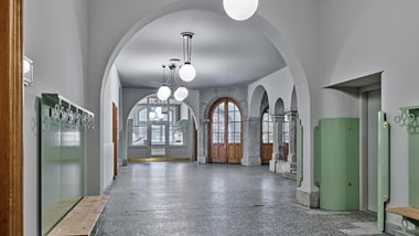Flur mit Bögen und grossen Fenstern, helle Lichtakzente.