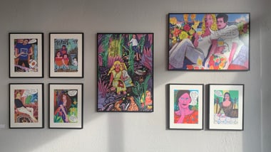 Galeriewand mit bunten, gerahmten Illustrationen.