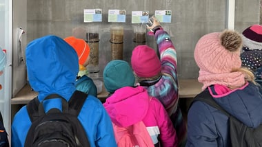 Kinder in bunten Jacken schauen sich Ausstellung an.