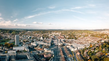 Luftaufnahme einer Stadt mit Gebäuden und Strassen bei klarem Himmel.