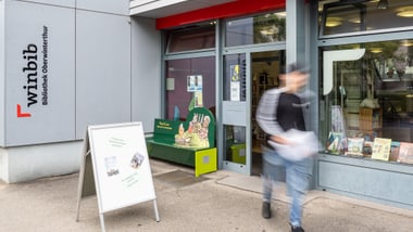 Aussenansicht Bibliothek Oberwinterthur. Person geht an Schaufenstern vorbei.