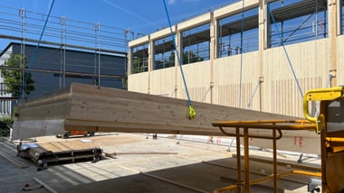 Holzbauteil wird mit Kran auf Baustelle gehoben.