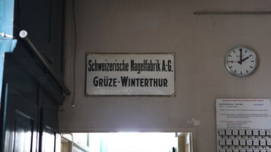 Schild und Uhr an der Wand eines Flurs.