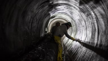 Zwei Personen arbeiten in einem Tunnel mit Taschenlampen.