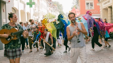 Menschen, die auf einer gepflasterten Strasse mit bunten Kostümen und Musikinstrumenten feiern.