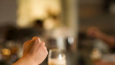 Hand gestikuliert an einer Bar mit einem Bierglas.