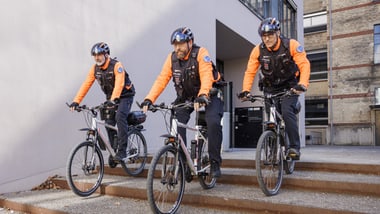 Drei Menschen in orangefarbener Kleidung fahren mit Fahrrädern eine Treppe hinunter.