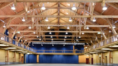 Grosser, leerer Holzsaal mit hoher Decke und blauen Vorhängen.