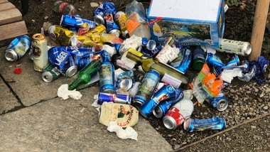 Haufen von leeren Getränkedosen und Flaschen auf dem Boden neben einem Weg.