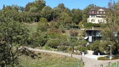 Hügelige Landschaft mit Häusern und Bäumen unter blauem Himmel.