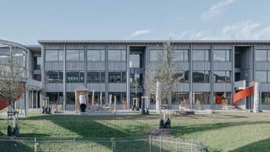 Moderne Schulgebäude mit Spielplatz im Vordergrund.