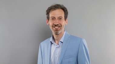 Mann in blauem Anzug vor grauem Hintergrund.