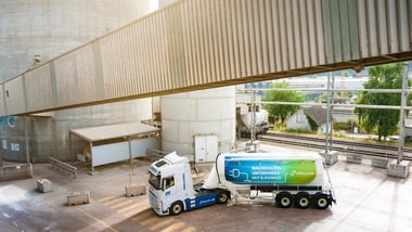 Lastwagen mit Anhänger auf Industriegelände neben Silotürmen.