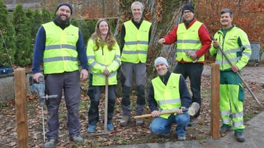 Sechs Personen in gelben Sicherheitswesten posieren vor einem Baum.