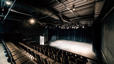 Kleiner leerer Theatersaal mit Bühne und Sitzreihen.