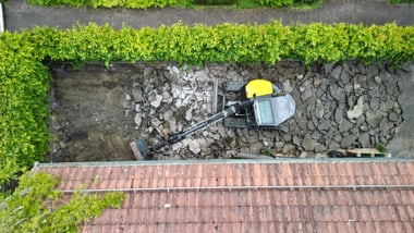 Luftaufnahme eines Baggers in einem Garten mit zerbrochenem Beton.