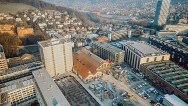 Luftaufnahme von Stadt mit Gebäuden und Hügeln im Hintergrund.