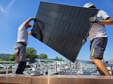 Zwei Personen installieren ein Solarpanel auf einem Dach.