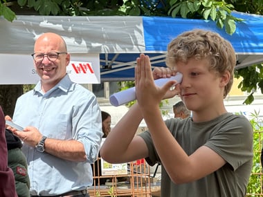 Ein Junge macht ein naturwissenschaftliches Experiment, während ein Mann in einem Hemd lächelt.