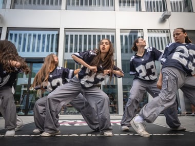 Fünf Tänzerinnen in sportlichen Outfits auf einer Bühne.
