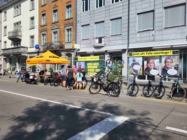 Strassenszene mit Personen unter einem gelben Zelt und Fahrräder aufgereiht.