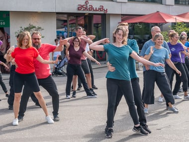 Gruppe von Menschen tanzt im Freien auf einer Strasse.