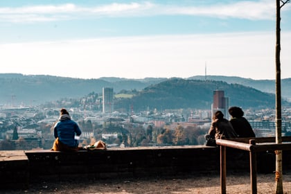 Menschen sitzen auf einer Mauer mit Stadtblick im Hintergrund.