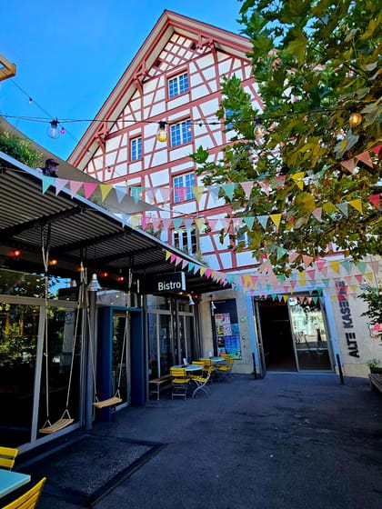 Aussenbereich eines Bistros mit bunten Wimpeln und Fachwerkgebäude.