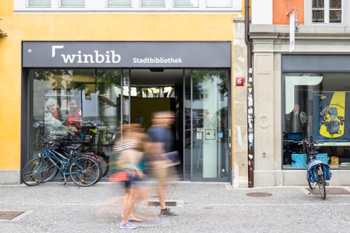 Aussenansicht der Stadtbibliothek mit gehenden Personen.