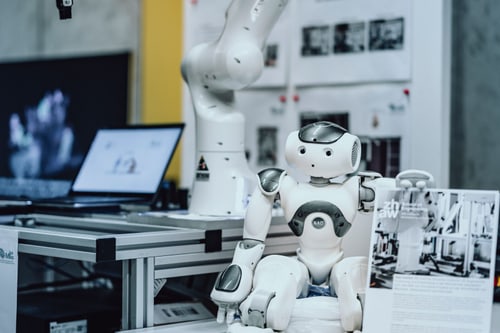 Roboter an einem Tisch mit einem mechanischen Arm im Hintergrund.