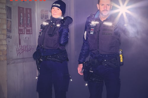 Zwei uniformierte Personen mit Taschenlampen in einem dunklen Raum.