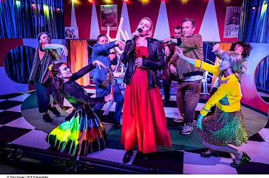 Gruppe von Menschen auf einer Bühne in bunter Kleidung tanzt und singt.