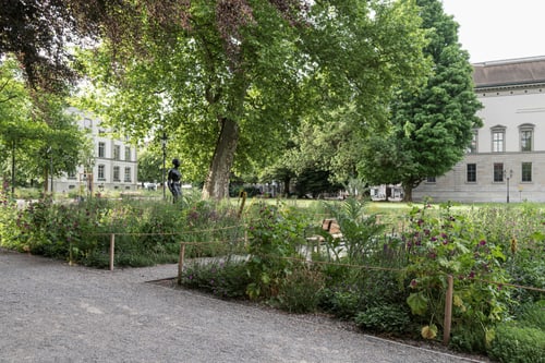 Garten mit Bäumen, Blumen und historischem Gebäude.