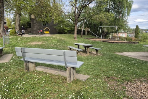 Spielplatz mit Schaukel, Bank und Bäumen.