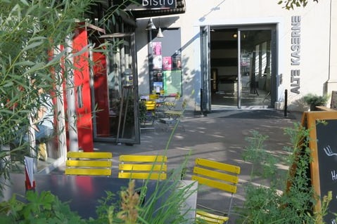 Gelbe Bistrostühle vor einem Gebäudeeingang mit Schildern und Pflanzen.