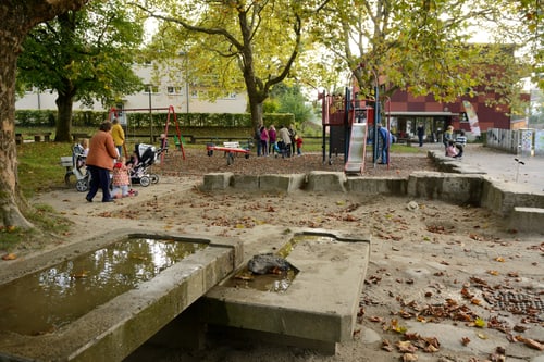 Kinder und Erwachsene in einem Spielplatz mit Spielgeräten und Bäumen.