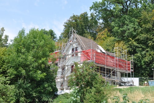 Haus im Bau mit Gerüst, umgeben von Bäumen.
