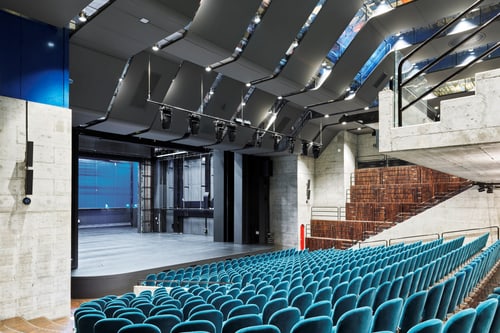Moderner Theatersaal mit blauen Stühlen und Bühne.