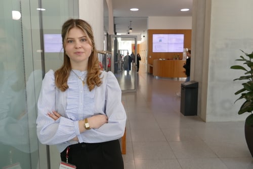 Person mit hellblauer Bluse steht in modernem Flur.