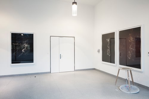 Galeriewand mit drei grossen Bildern und einem Hocker.