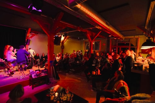 Beleuchteter Konzertsaal mit Publikum und Musikern auf der Bühne.