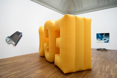 Gelbe aufblasbare Skulptur in einer Galerie mit Holzboden.