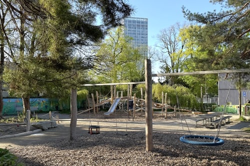 Spielplatz mit Klettergerüst und Bäumen im Hintergrund.