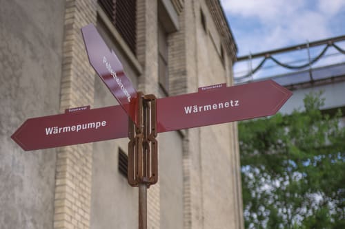 Wegweiser mit rotem Pfeil vor einem Gebäude.