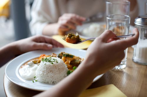 Personen essen an einem Tisch Reisgericht mit Gemüse.