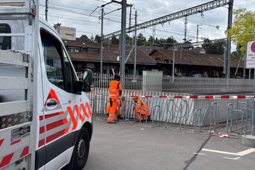 Zwei Personen in orangefarbener Kleidung arbeiten neben einem Fahrzeug mit rot-weissen Markierungen.