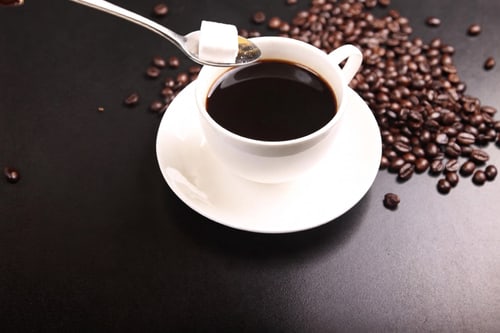 Tasse Kaffee mit Zuckerwürfel auf einem Löffel und Kaffeebohnen.