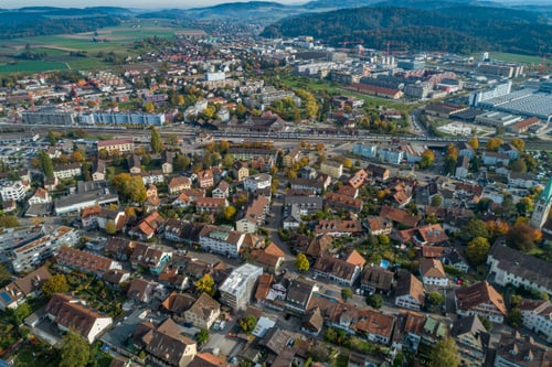 Luftaufnahme einer Stadt mit Häusern, Strassen und grünen Feldern im Hintergrund.