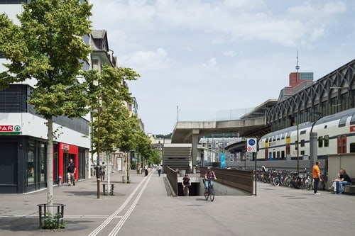 Ausfahrt der Velounterführung am Bahnhof Winterthur mit Geschäften, Fahrradfahrern und einem Zug.