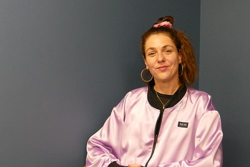 Person mit lila Jacke vor einer blauen Wand.